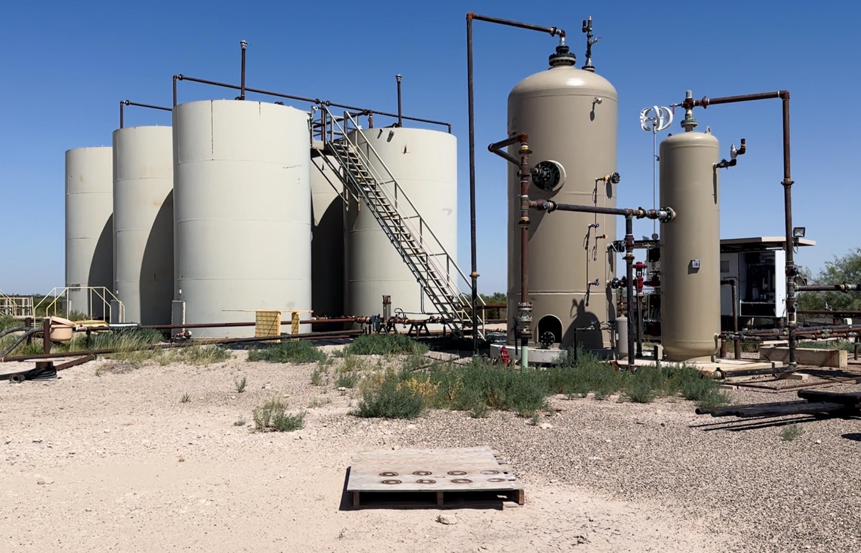 Detail of production equipment on a working site: two vertical separator vessels with valves, gauges and connecting pipework, beside a control cabinet.