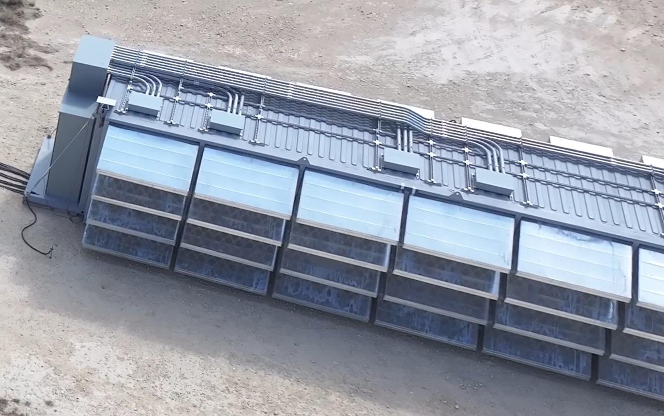 Close aerial view of open-top immersion-cooling tanks filled with dielectric fluid, with distribution pipework running along the top of the row.